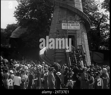 Eine Fahrt auf dem Helter Skelter Fairground in einem Park mit einem Mann am Eingang mit einem Megaphon, bevor eine große Menschenmenge die Leute beobachtete, die die Fahrt hinunter rutschen, 1939. Aus „Time to Remember – The Reluctant Warriors“, 1939 (Reel 1); Dokumentarfilm über Ereignisse von 1939 – Vorbereitungen für den Krieg und dann Feindseligkeiten brechen aus. Stockfoto