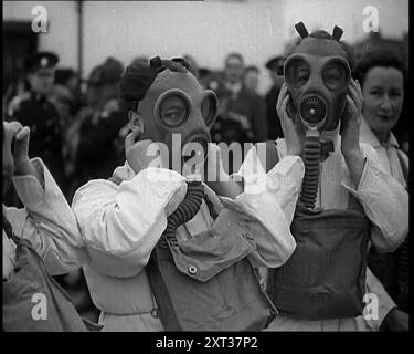 Eine Nahaufnahme von drei weiblichen Zivilverteidigern in weißen Kesselanzügen, die Gasmasken mit Männern im Hintergrund tragen, 1938. Aus „Time to Remember – Wind Up Week“, 1938 (Reel 2); Dokumentarfilm über 1938 – die Menschen werden sich der wachsenden Bedrohung des Krieges bewusst. Stockfoto