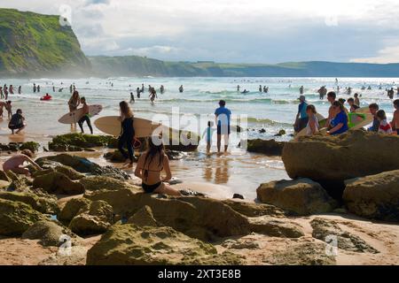 Surfer mit Surfbrettern spazieren entlang des felsigen Surferstrands Playa de los Locos an einem heißen Juli-Tag Suances Cantabria Spanien Europa Stockfoto