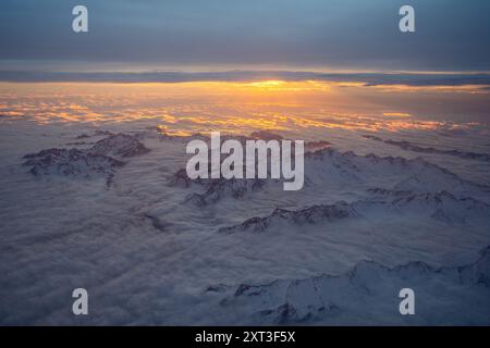 Ein atemberaubender Blick auf einen sonnendurchfluteten Himmel über den schneebedeckten Gipfeln der Schweizer Alpen, der bei Sonnenaufgang von den Wolken erfasst wird Stockfoto