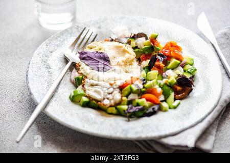 Ein nahrhaftes Keto-freundliches Mittagessen mit einem frisch gekochten Ei auf einem bunten gemischten Salat mit Gurken, Tomaten und violettem Basilikum, serviert auf einer Ma Stockfoto