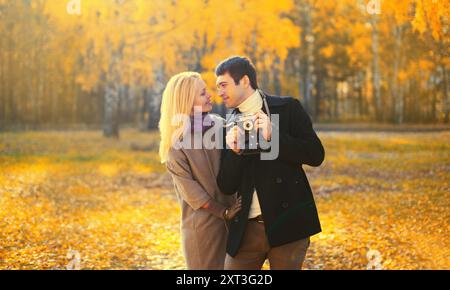 Glückliches, liebevolles junges Paar, das mit der Filmkamera im Herbstpark an einem warmen sonnigen Tag fotografiert Stockfoto