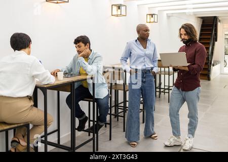 In einer englischen Akademie arbeitet eine Gruppe von Fachleuten zusammen, die an Diskussionen teilnehmen und Laptops in einem modernen, gut beleuchteten Raum nutzen Stockfoto