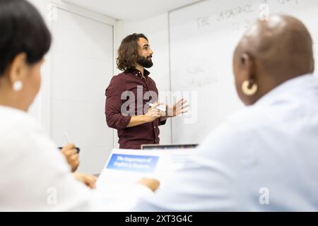 Eine vielfältige Gruppe erwachsener Lerner nimmt an einem Englischunterricht in einem modernen Schulungsraum Teil, der von einem enthusiastischen männlichen Lehrer geleitet wird Stockfoto