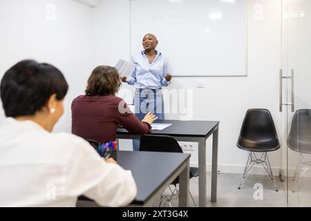 Eine junge schwarze Lehrerin steht vor einer vielfältigen Gruppe von erwachsenen Schülern in einer Englischstunde und gibt energisch Erklärungen und Schwäche Stockfoto
