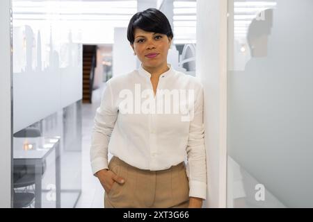 Eine professionelle Frau in weißem Hemd steht selbstbewusst in einem modernen Büroumfeld und symbolisiert Führungsstärke und Fachwissen, ideal für die Darstellung von Themen zu Stockfoto