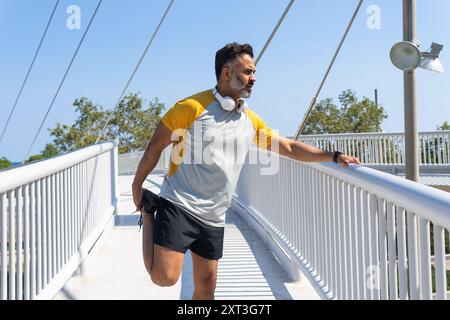 Indischer männlicher Sportler, der an einem hellen, sonnigen Tag eine Pause einlegt und von der Kamera wegblickt, mit Kopfhörern um den Hals. Stockfoto