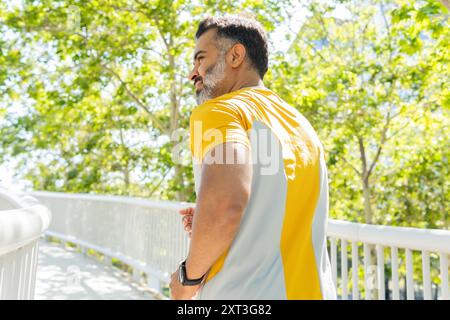 Rückansicht eines Indianers, gekleidet in einem gelben Sportrikot, Joggen in einem sonnigen Park. Er blickt von der Kamera weg und genießt eine erfrischende Outdoor-Übung Stockfoto