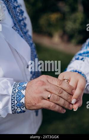 Braut und Bräutigam in ukrainischer Kleidung mit Bändern, die während der Hochzeitszeremonie die Hände halten Stockfoto