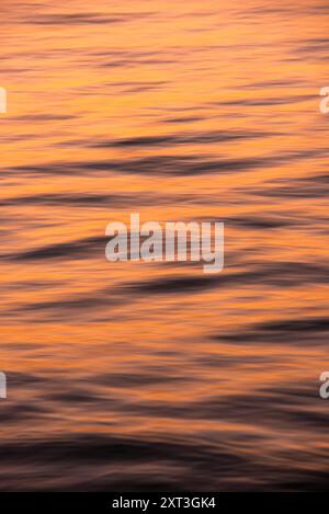 Dieses Bild fängt die ruhige Schönheit des Ozeans bei Sonnenuntergang mit sanften Wellen in goldenen Tönen ein, die eine ruhige, ruhige Atmosphäre schaffen Stockfoto