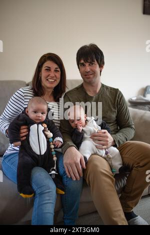 Eine fröhliche vierköpfige Familie mit Eltern und ihren Zwillingskindern genießt einen gemeinsamen Moment auf einem Sofa in einer warmen, einladenden Atmosphäre Stockfoto