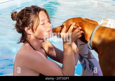 Eine junge Frau im Badeanzug teilt einen fröhlichen Moment mit ihrem braunen Hund am Pool und unterstreicht die besondere Verbindung zwischen Mensch und Haustier Stockfoto