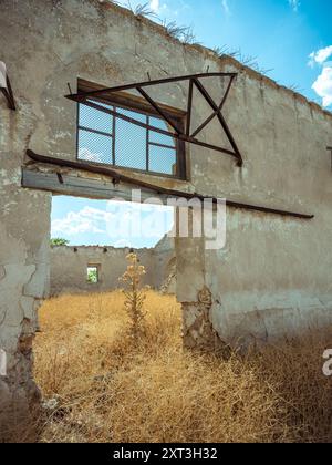 Blick von der Sonne auf ein einsames Gebäude mit bewachsenem, getrocknetem Gras und verfallenen Wänden vor einem leuchtend blauen Himmel. Stockfoto