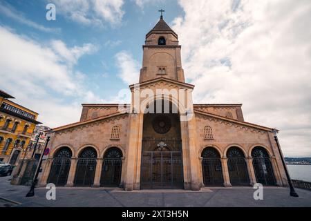 Majestätischer Blick auf eine traditionelle Kirchenfassade in Gijon, Spanien, mit historischer Architektur vor einem dramatisch bewölkten Himmel. Stockfoto