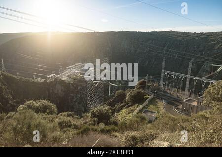Dieses Bild, das im warmen Glanz des Sonnenlichts aufgenommen wurde, zeigt ein ruhiges Wasserkraftwerk auf dem spanischen Hügel mit einer Hochspannungsleitung Stockfoto