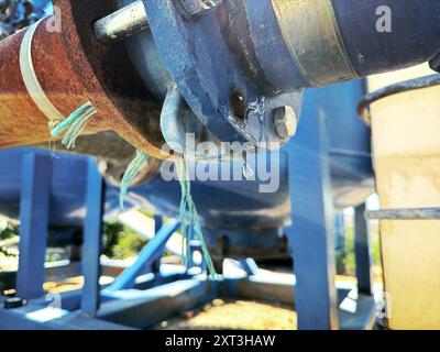 Nahaufnahme eines Wassertropfens, der sich an der Verbindung eines großen Industrierohrs bildet und Wasserverschwendung in Bewässerungs- und Industriesystemen symbolisiert Stockfoto