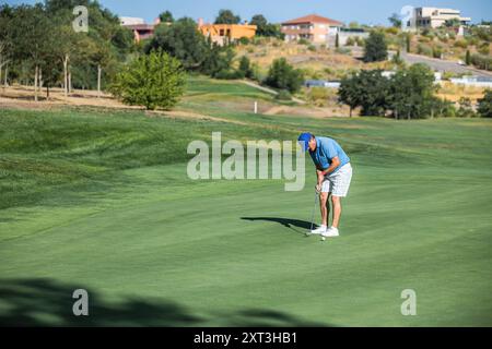 Ein Golfspieler mittleren Alters in einem blauen Poloshirt und weißen Shorts spielt intensiv Golf. Vor einer üppigen, sonnigen Kulisse konzentriert er sich auf Stockfoto