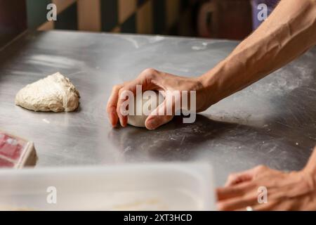 Ein Nahaufnahme-Bild, das die Hände eines Küchenchefs beim Kneten von Pizzateig auf einer Metalltheke zeigt und die frühen Phasen der Pizzazubereitung zeigt Stockfoto