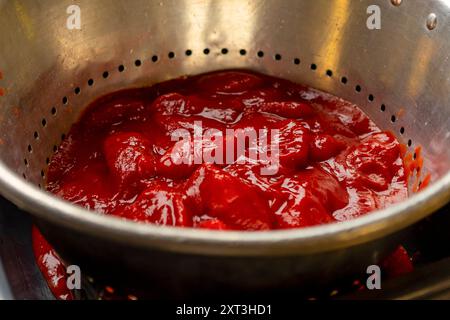 Hell-rote Tomatensoße, reichhaltig und klobig, sitzt in einem metallischen Sieb und unterstreicht die frühen Phasen des Kochens einer hausgemachten Pizza Stockfoto