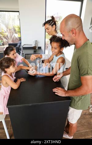 Eine vielfältige Familie macht sich glücklich mit dem Keksbacken in einer modernen Küche Eltern und kleine Kinder, einschließlich Töchter, teilen einen freudigen Moment Stockfoto