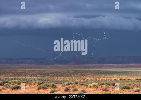 Ein mächtiger Sturm, der dunkle Wolken wirft, entfesselt einen eindrucksvollen Blitz über die berühmte rote Wüstenlandschaft des Monument Valley Stockfoto