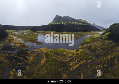 Ein ausgedehnter Luftschuss über die üppigen, nebeligen Landschaften des isländischen Highlands mit schroffen Bergen, die mit lebhaftem grünem Moos und Ser verwoben sind Stockfoto