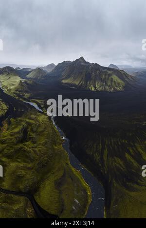 Ein beeindruckendes Luftbild zeigt die raue Schönheit des isländischen Hochlands mit zerklüfteten grünen und schwarzen Bergen unter einem stimmungsvollen Himmel Stockfoto
