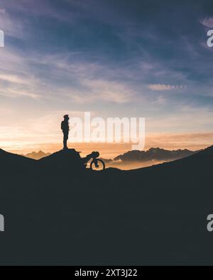 Ein Radfahrer steht neben seinem Fahrrad, die Silhouette vor einem spektakulären Sonnenuntergang auf dem zerklüfteten Gelände der Berge Curavacas und Espiguete in Palencia Stockfoto