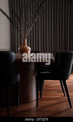 Eine schicke Einrichtung mit modernem Esstisch und Stühlen, die auf strukturierten Vorhängen stehen, mit einer Terrakotta-Vase und getrockneten Zweigen, die einen Hauch von n verleihen Stockfoto