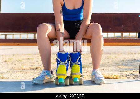 Fangen Sie den Moment ein, in dem eine junge Frau auf einer Bank sitzt und ihre leuchtend blauen und gelben Rollschuhe vor einem sonnigen Hintergrund im Freien schnürt Stockfoto