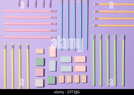 Draufsicht auf ordentlich organisierte Schulmaterialien auf violettem Hintergrund, einschließlich rosa, blauer, gelber und grüner Bleistifte, und verschiedene klebrige nicht Stockfoto