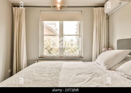 Helles und luftiges, modernes Schlafzimmer mit großem Fenster mit Aussicht, neutralen Farben und einem gemütlichen Bett. Stockfoto