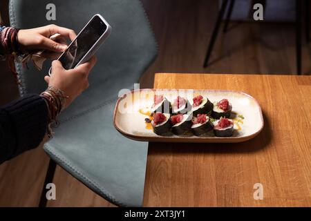 Eine Person nimmt ein Foto von frisch zubereiteten Sushi-Brötchen mit Thunfisch auf einem Designer-Teller auf und zeigt die Kunst der Lebensmittelfotografie Stockfoto