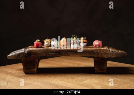 Ein elegantes Sushi-Sortiment, wunderschön auf einer rustikalen hölzernen Sushi-Platte angeordnet, vor dunklem Hintergrund. Die Auswahl umfasst Nigiri und Uni Stockfoto