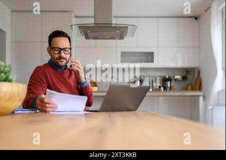 Seriöser Geschäftsmann, der Finanzdokumente telefonisch diskutiert, während er vom Home Office aus arbeitet Stockfoto