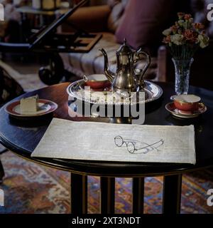 viktorianische Kaffeekanne mit zwei Tassen Kuchenzeitung und Lesebrille auf Couchtisch Stockfoto