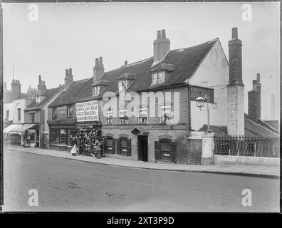 Old Bull Public House, Wandsworth High Street, Wandsworth, Greater London Authority, 1900. Das Old Bull Public House und die angrenzenden Geschäfte an der Wandsworth High Street 78-82 aus südwestlicher Sicht. Der Schuh- und Schuhladen in der Mitte dieser Reihe trägt ein Banner mit der Aufschrift: "GEBÄUDE KOMMEN, ZWANGSVERKAUF - GROSSE SCHNÄPPCHEN - ALLE WAREN MÜSSEN ABGERÄUMT WERDEN". Anfang des 20. Jahrhunderts wurden die hier gezeigten Gebäude abgerissen und durch eine dreistöckige Terrasse mit Geschäften ersetzt, die einen neuen Bull Pub enthielt. Der neue Bull Pub wurde während des Zweiten Weltkriegs durch Bombenangriffe verloren, aber das angrenzende Geschäft wurde gebaut Stockfoto