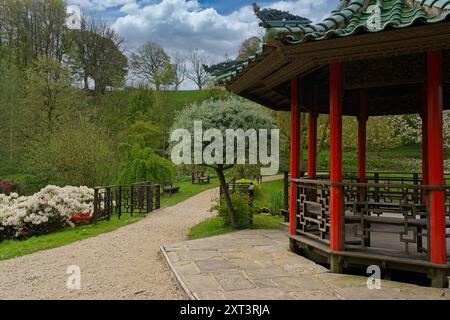 Ein gewundener Pfad, der sich durch üppiges Grün schlängelt und mit hellen Blumen und einer traditionellen Pagode in Grewelthorpe, North Yorkshire, Großbritannien, dekoriert ist. Stockfoto