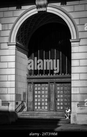 Eine junge tätowierte Frau sitzt auf den Stufen des alten Martins Bank-Gebäudes in Liverpool und liest ihr Handy Stockfoto