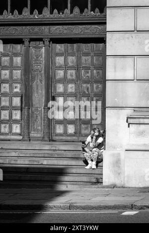 Eine junge tätowierte Frau sitzt auf den Stufen des alten Martins Bank-Gebäudes in Liverpool und liest ihr Handy Stockfoto