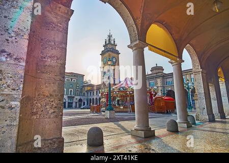 Der hohe Stein-Gedenkturm und das Vintage-Karussell vom Säulengang des Piacentiniano Centre, Piazza Vittorio Veneto, Citta Bassa, Bergamo, Italien Stockfoto