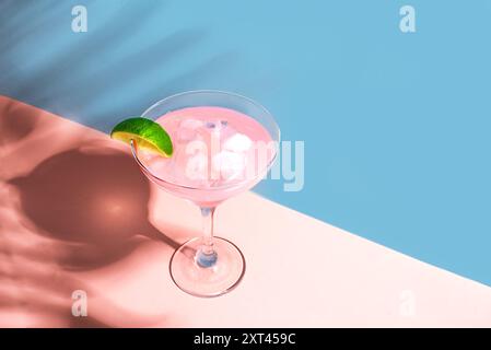 Rosa Margarita oder Daiquiri Cocktail im Glas mit Limette auf rosa und blauem Hintergrund mit Palmblattschatten, Kopierraum. Konzept einer Cocktail-Strandparty, Stockfoto