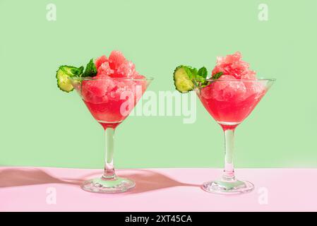 Wassermelonen Slushie oder Granita Cocktail Drink mit Minze in zwei Gläsern auf rosa und grünem trendigen Hintergrund. Erfrischendes kaltes, im Sommer rasiertes Eisgetränk oder Stockfoto