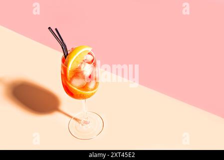 Aperol Spritz Cocktail im Glas mit orangefarbenen Scheiben auf rosa pfirsichfarbenem Hintergrund, Kopierraum, trendiges hartes Licht. Alkohol Aperol Spritz Aperetivo. Stockfoto