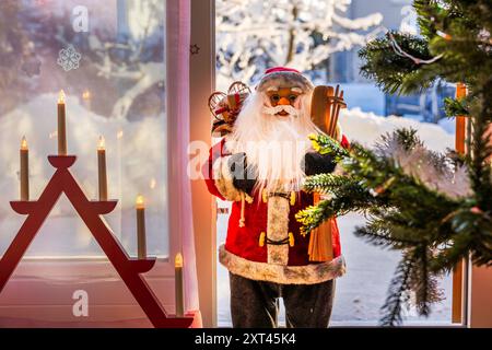 Blick auf die Innenausstattung des Zimmers mit Weihnachtsmann und elektrischem Adventskerzenhalter vor Panoramafenstern mit Blick auf den verschneiten Villengarten. Schweden. Stockfoto