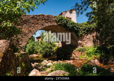 Eine historische Steinbrücke erhebt sich anmutig über einen ruhigen Bach in Hervas, Caceres. Umgeben von üppigem Grün und getaucht in flauschigem Sonnenlicht, ist es ca. Stockfoto