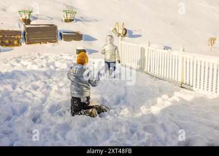 Nahaufnahme von zwei Kindern, die mit Schneebällen im Hinterhof der Villa am sonnigen, frostigen Wintertag spielen. Schweden. Stockfoto