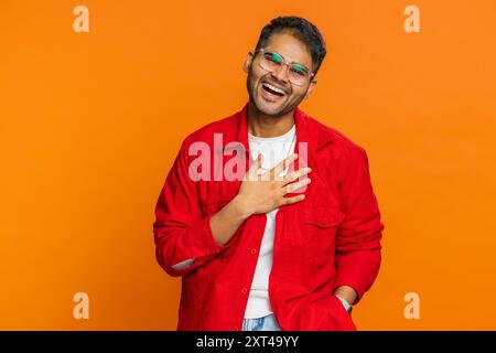 Glücklicher junger indischer Mann, der laut lacht, nachdem er lächerliche Anekdoten gehört hat, Reaktion auf lustigen Witz, unbeschwert amüsiert. Positiver Lebensstil. Arabischer Typ isoliert auf Studio-orange Hintergrund Stockfoto