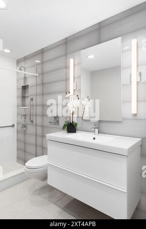 Ein Badezimmer mit einem weißen Schrank, einer rechteckigen Wand aus grauem Glas und einer Dusche mit Chromarmatur und Nische. Stockfoto