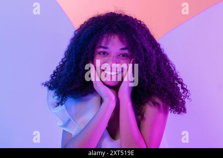 Nahporträt einer lächelnden Afrikanerin in weißem Kleid. Süßes schwarzes, lockiges Mädchen posiert im Studio. Entspannter und glücklicher Teenager. Neonfarben Stockfoto